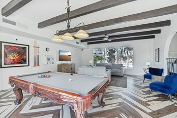 A pool table is in the middle of a room with a blue chair to the right.
